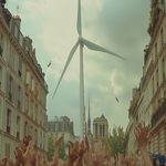 Éolienne géante au milieu de manifestants dans une rue de Paris, illustrant la transition énergétique et les enjeux sociaux