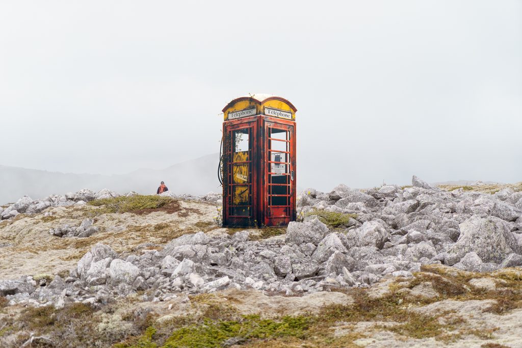 Rustic red telephone booth standing alone on rocky terrain in a misty, desolate landscape